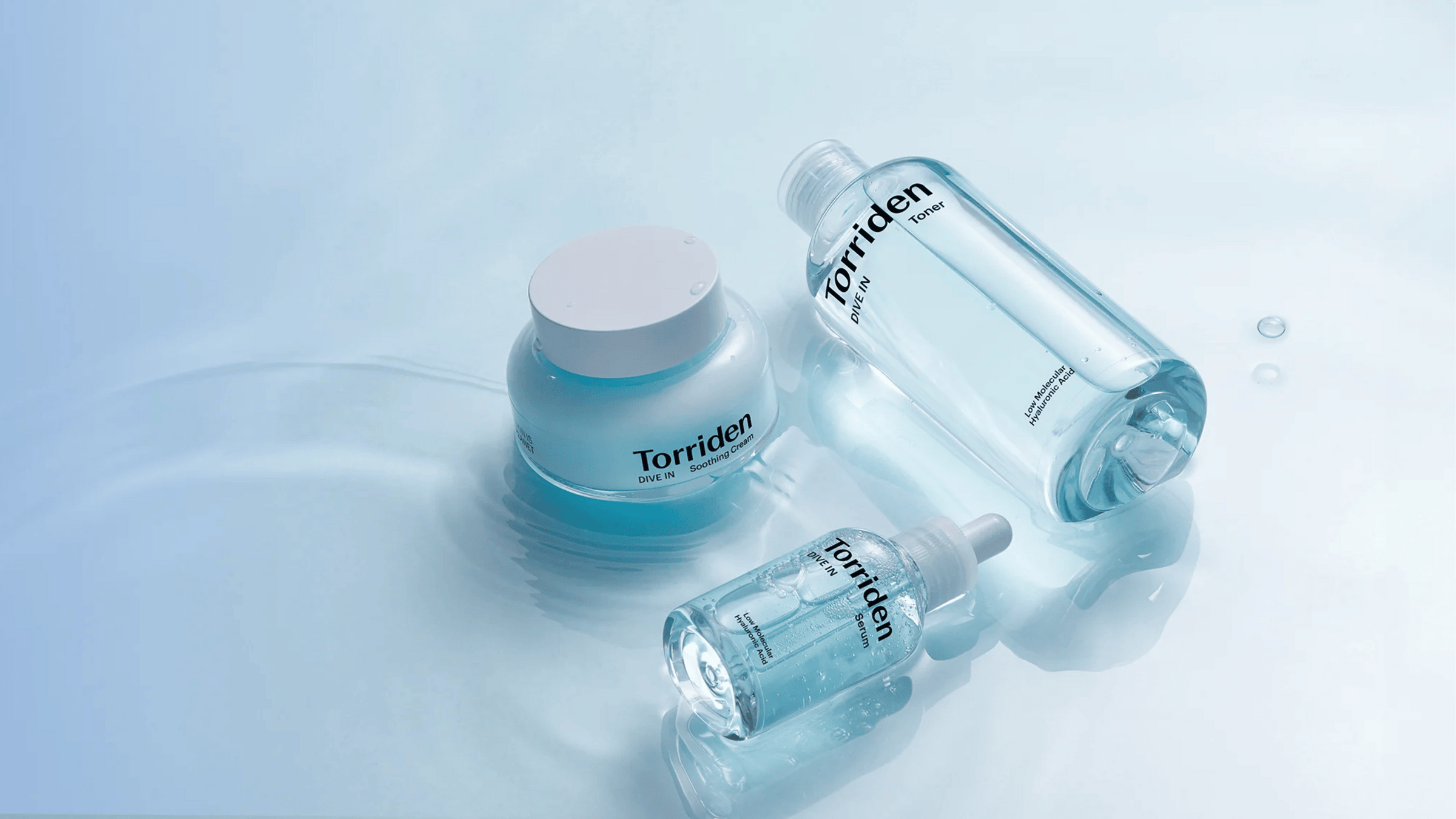 En trio av Torriden DIVE IN-produkter: toner, serum och soothing cream, visas på en vattenliknande yta. De ljusblå förpackningarna förstärker känslan av återfuktning och fräschör, med fokus på hyaluronsyrans intensiva fuktgivande egenskaper.