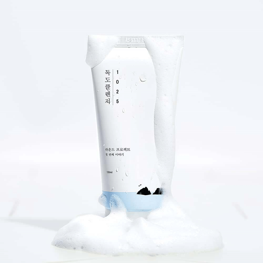 1025 Dokdo Cleanser in weißer Tube, bedeckt mit Schaum, mit Wasserperlen und Schaum um den Boden, freigestellt vor hellem Hintergrund.