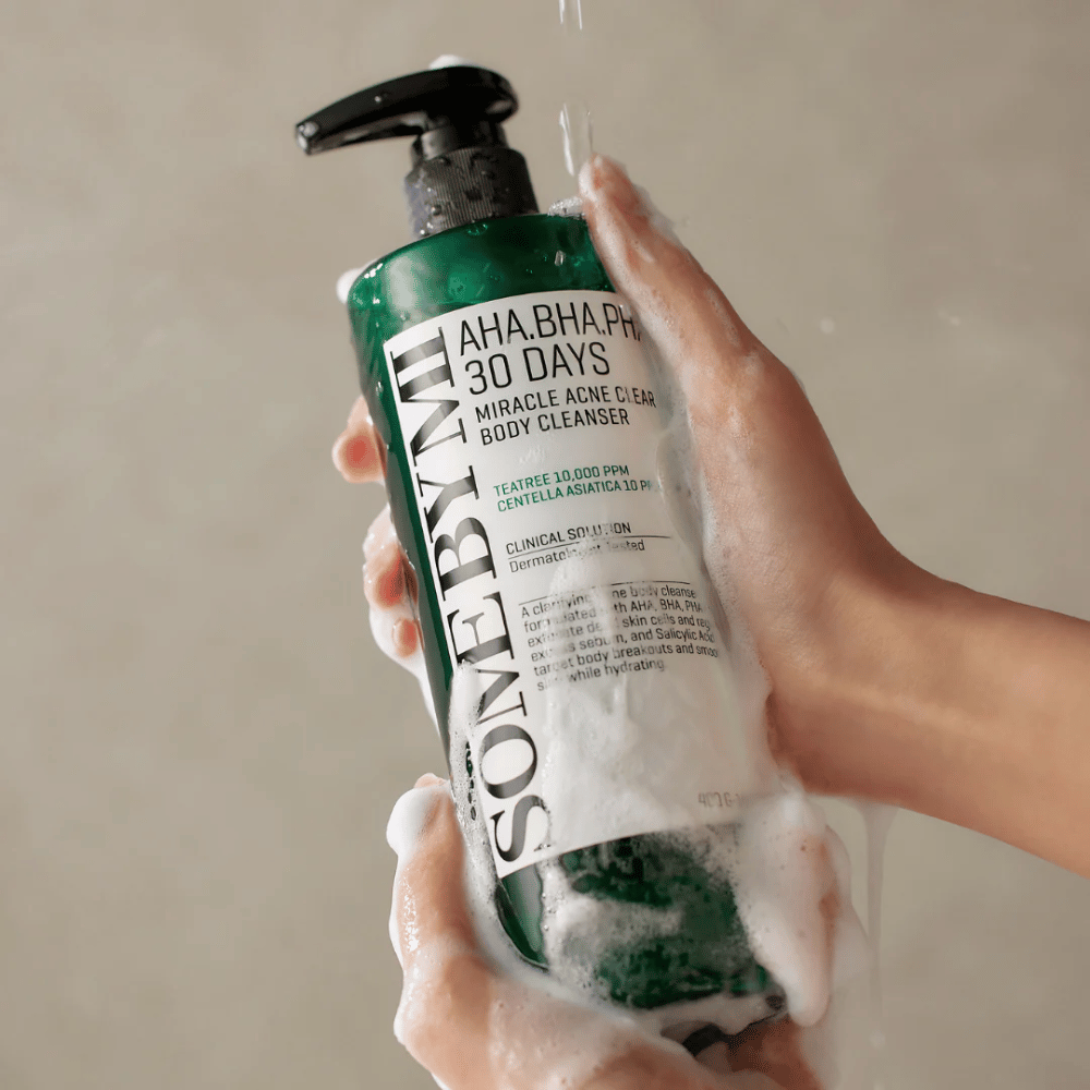 Eine Person hält eine Flasche SOME BY MI AHA.BHA.PHA 30 Days Miracle Acne Clear Body Cleanser. Die Flasche ist grün mit einem weißen Etikett und ist mit Schaum des Reinigungsmittels bedeckt. Die Person wäscht sich mit dem Produkt, während Wasser über die Hände fließt.