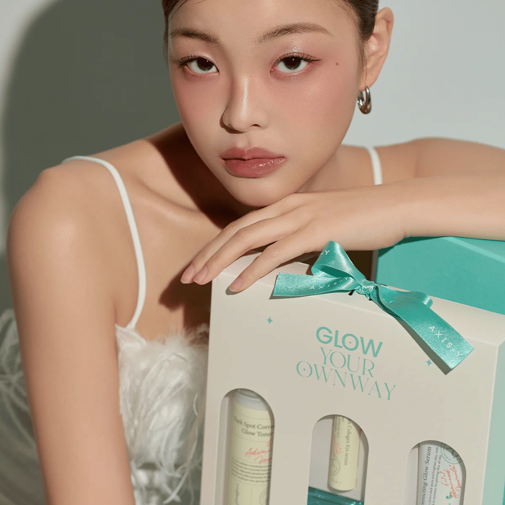 Modell mit elegantem Make-up hält in AXIS-Y:s „Glow Your Own Way“-Geschenkbox – ein stilvolles Hautpflegeset, perfekt als Geschenk für dich selbst oder jemanden, den du magst.
