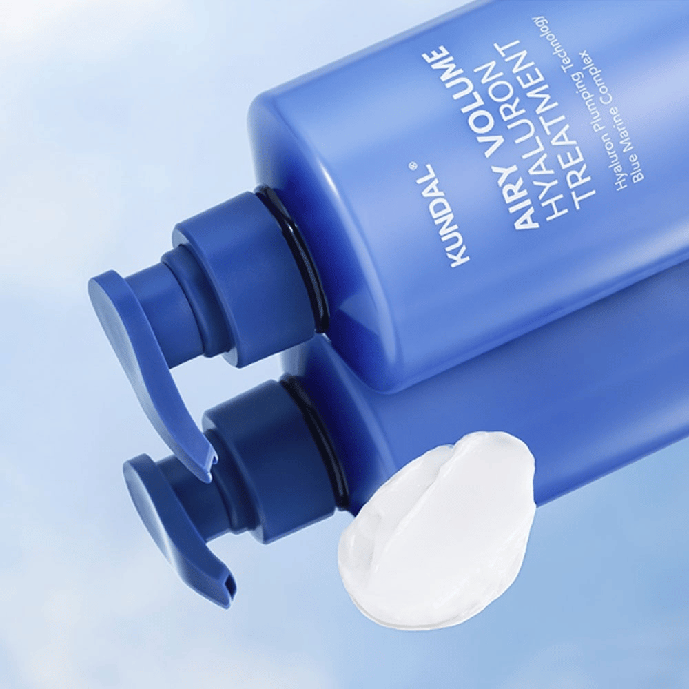 KUNDAL Airy Volume Hyaluron Treatment in blauer liegender Pumpflasche, mit sichtbarem weißen Cremeprodukt daneben.
