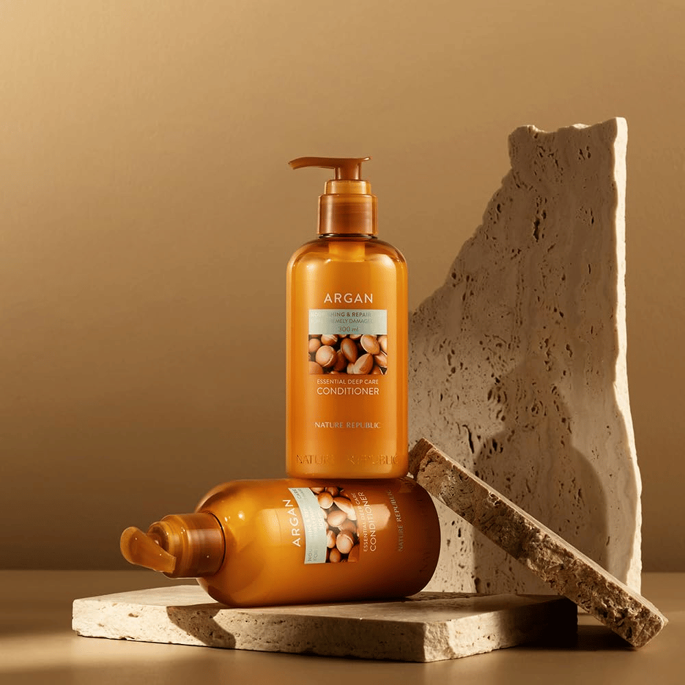 Zwei Flaschen von Nature Republic Argan Essential Moisture Repairing Conditioner auf einem warmen Steinuntergrund.