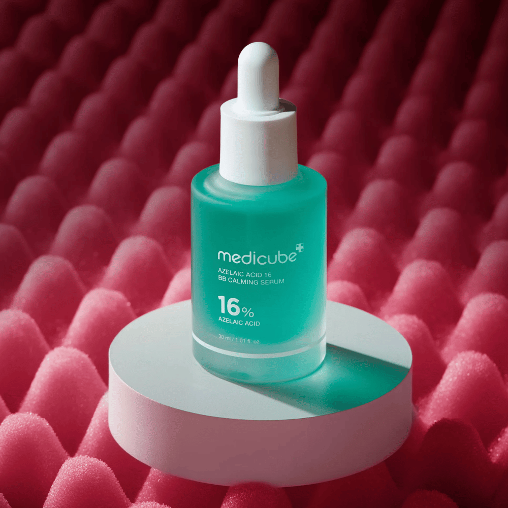 Produktbild von Medicube Azelaic Acid 16 BB Calming Serum auf einer weißen Podestfläche mit rosa strukturiertem Hintergrund, der das beruhigende und hautverbessernde Profil des Serums hervorhebt.