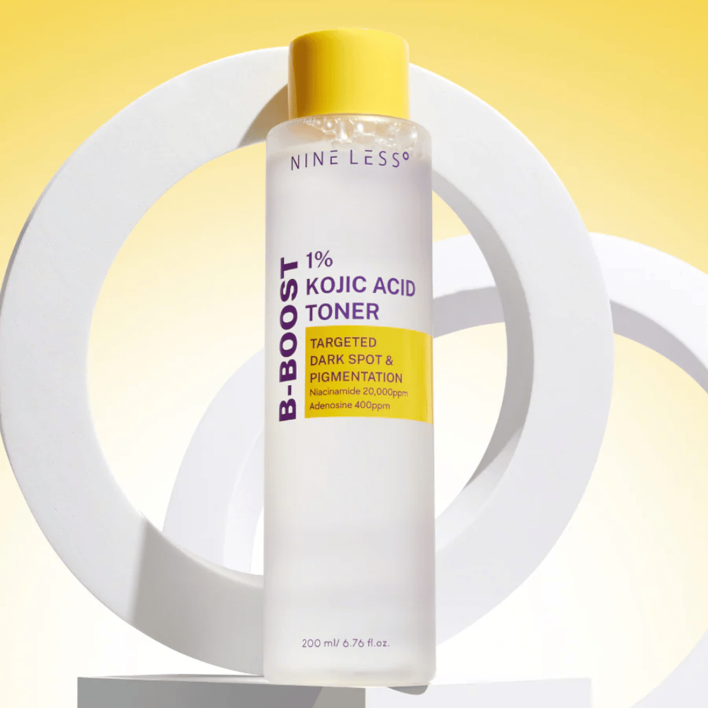 NINE LESS B-Boost 1% Kojic Acid Toner stehend vor gelbem Hintergrund mit dem Text "Targeted Dark Spot & Pigmentation". Hauttönungsausgleichender Toner mit Niacinamid und Adenosin.