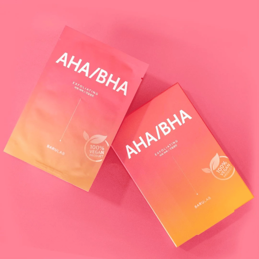 Zwei Produkte von BARULAB, eines in einer Tüte und eines in einem Karton, beide mit "AHA/BHA" und "Exfoliating" auf einem rosa Hintergrund gekennzeichnet. Die Produkte sind als "100% Vegan Product" markiert.