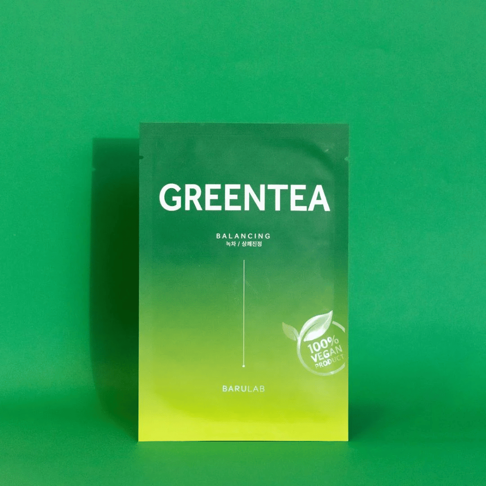 Eine Verpackung von BARULAB für eine "GREENTEA Balancing" Maske, markiert als "100% Vegan Product". Die Farbe der Verpackung wechselt von Dunkelgrün oben zu hellerem Grün unten, vor einem einheitlich grünen Hintergrund.