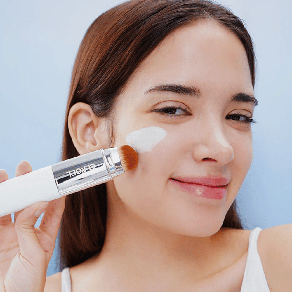 Model trägt ELROEL Blanc Cover Cream Stick concealer mit integriertem Pinsel auf die Wange auf für eine natürliche und gleichmäßige Deckkraft.
