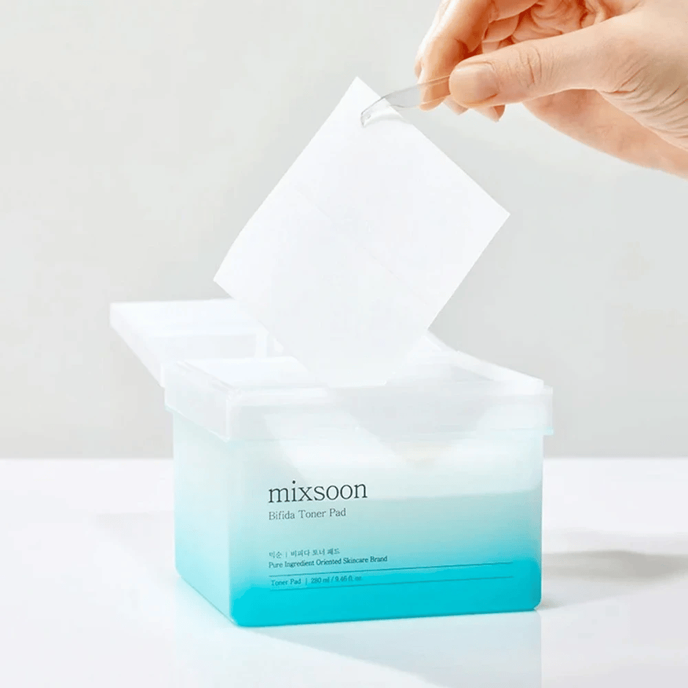 Ein transparenter Behälter mit einem blau-weißen Farbverlauf, der Bifida-Toner-Pads enthält. Eine Hand nimmt ein Toner-Pad aus dem Behälter, der mit "mixsoon Bifida Toner Pad" gekennzeichnet ist und 280 ml (9,46 fl. oz.) Toner-Pads für die Hautpflege enthält.