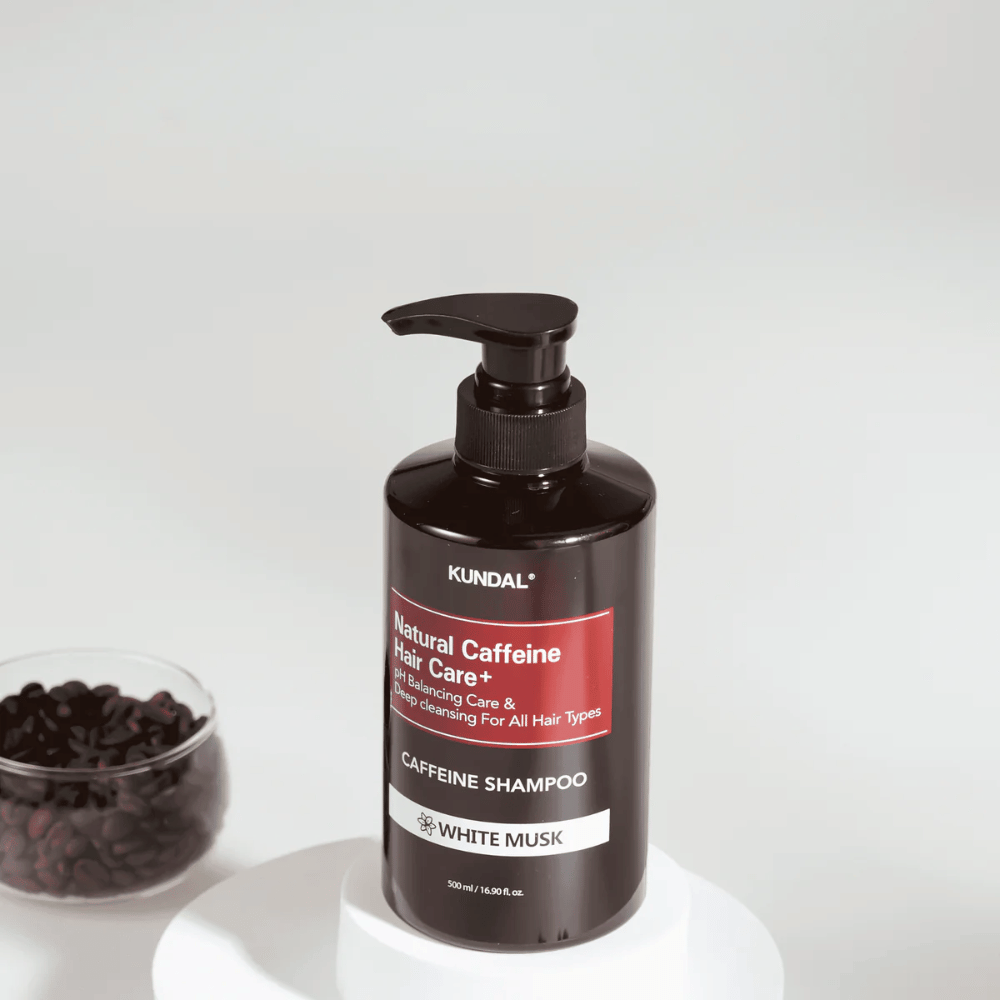 KUNDAL Natural Caffeine Hair Care+ Shampoo White Musk in schwarzer Pumpflasche, 500 ml, neben einer Schüssel mit Kaffeebohnen platziert.