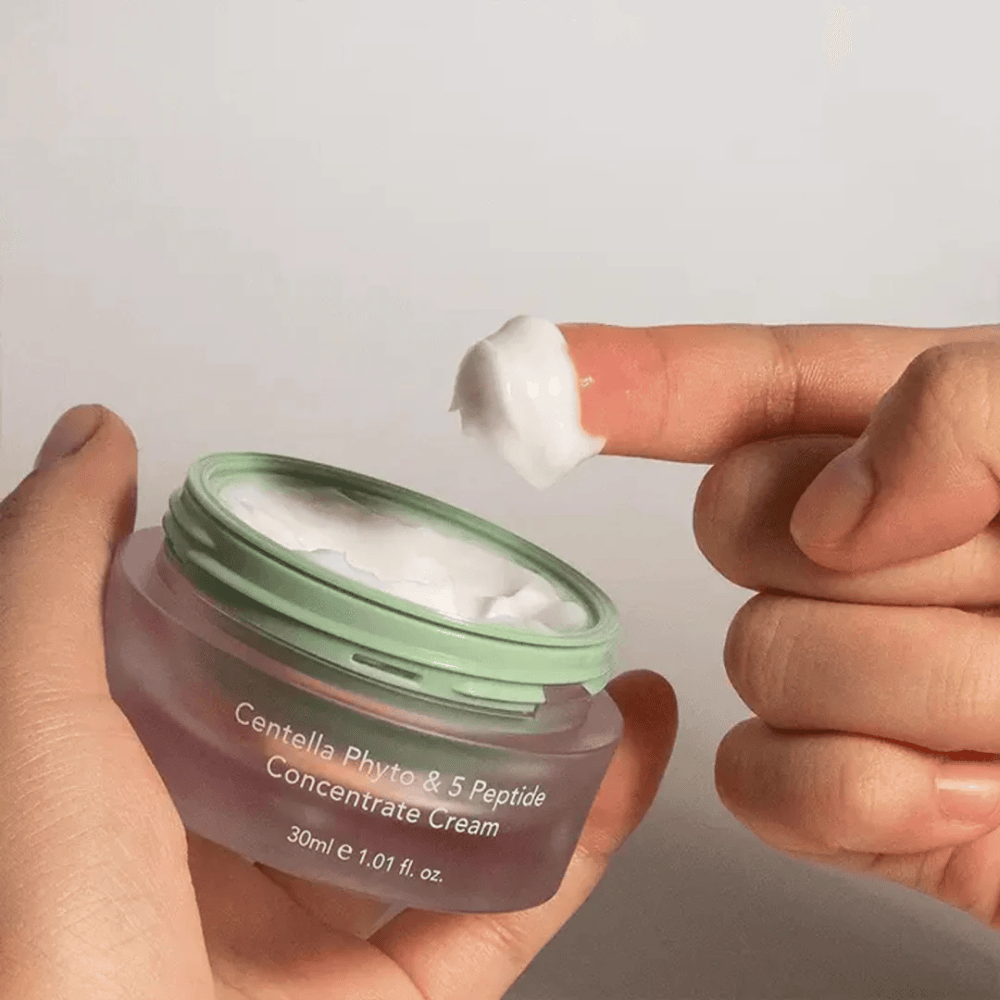 Hand, die einen Klecks Centella Phyto & 5 Peptide Concentrate Cream aus einer Dose nimmt.
