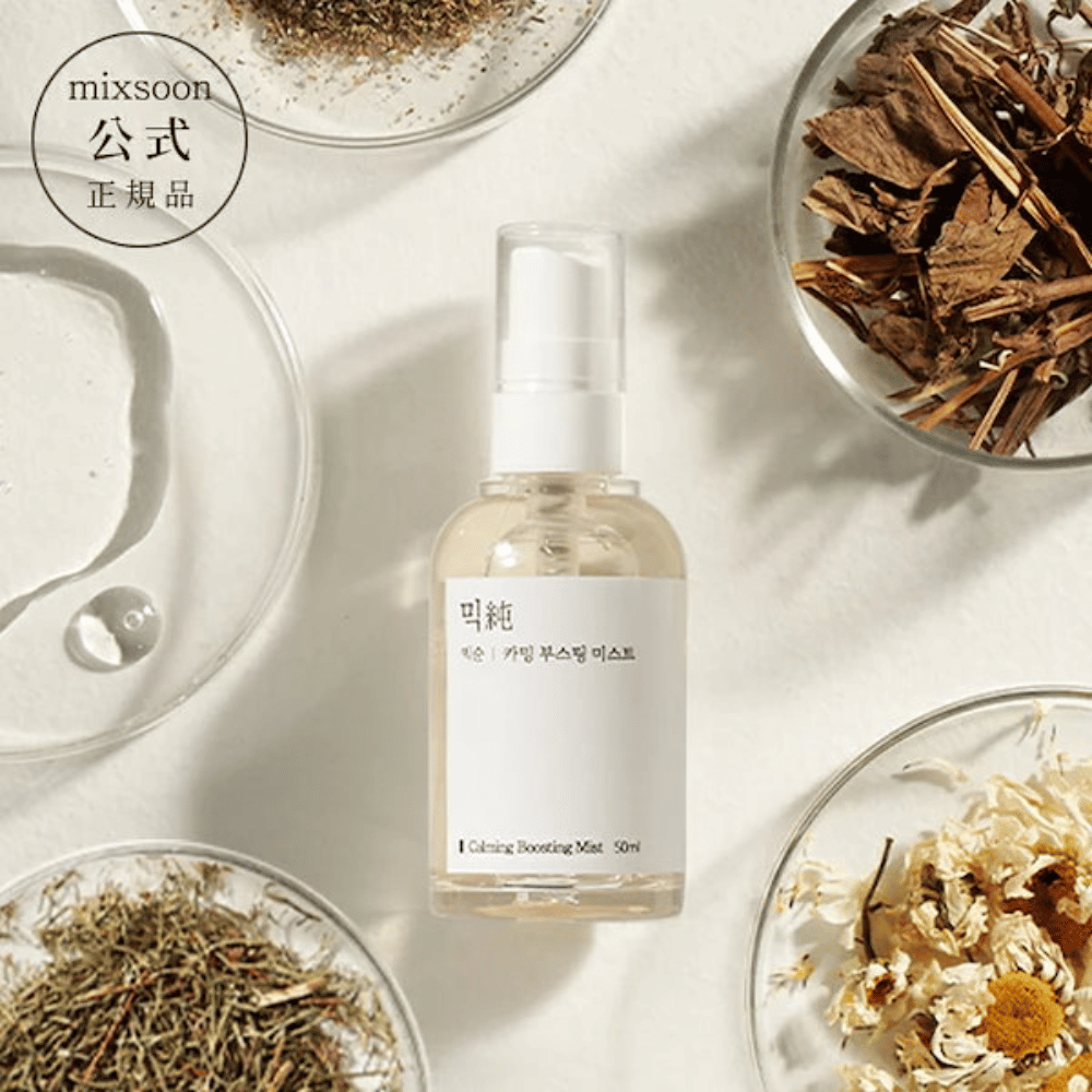 Eine durchsichtige Sprühflasche mit dem Etikett 'Calming Boosting Mist' von Mixsoon, umgeben von getrockneten Kräutern und Blumen auf weißen Schalen vor einem beigen Hintergrund, was die natürlichen Inhaltsstoffe der Produkte hervorhebt.