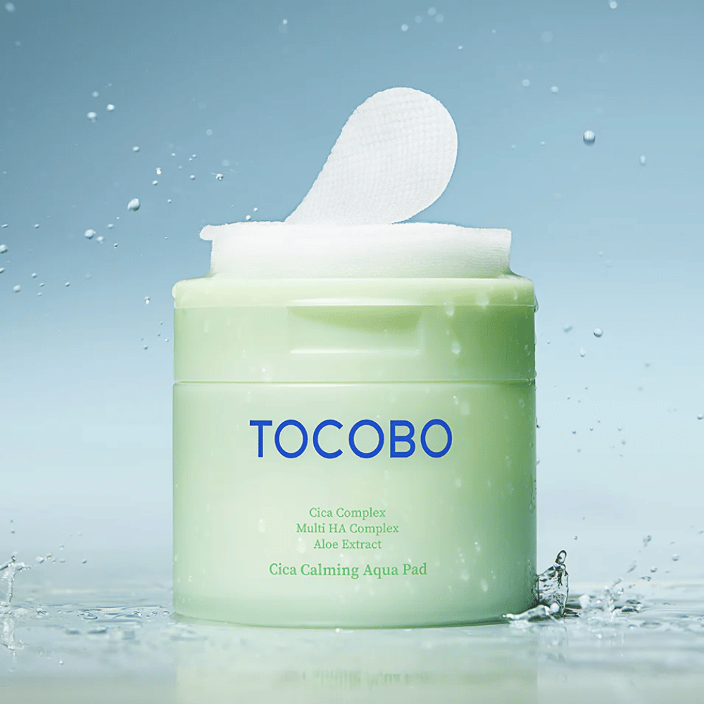 Geöffneter Behälter mit TOCOBO Cica Calming Aqua Pad, bei dem ein gesichtswasser Pad aus der Verpackung herausragt. Wassertropfen rund um das Produkt verstärken das Gefühl intensiver Feuchtigkeit und Frische.