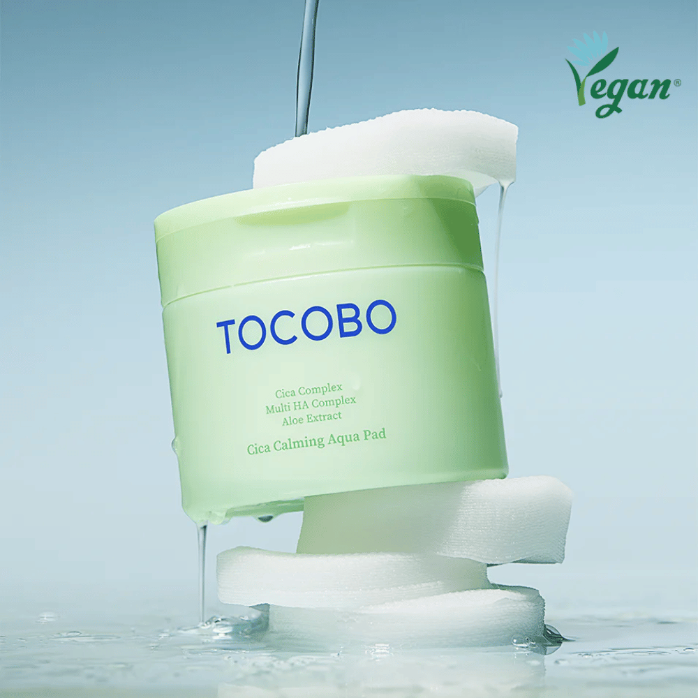 TOCOBO Cica Calming Aqua Pad zwischen toner pads mit fließender Essenz platziert. Das Vegan-Symbol betont die vegane Formulierung des Produkts und sein hautfreundliches Profil.