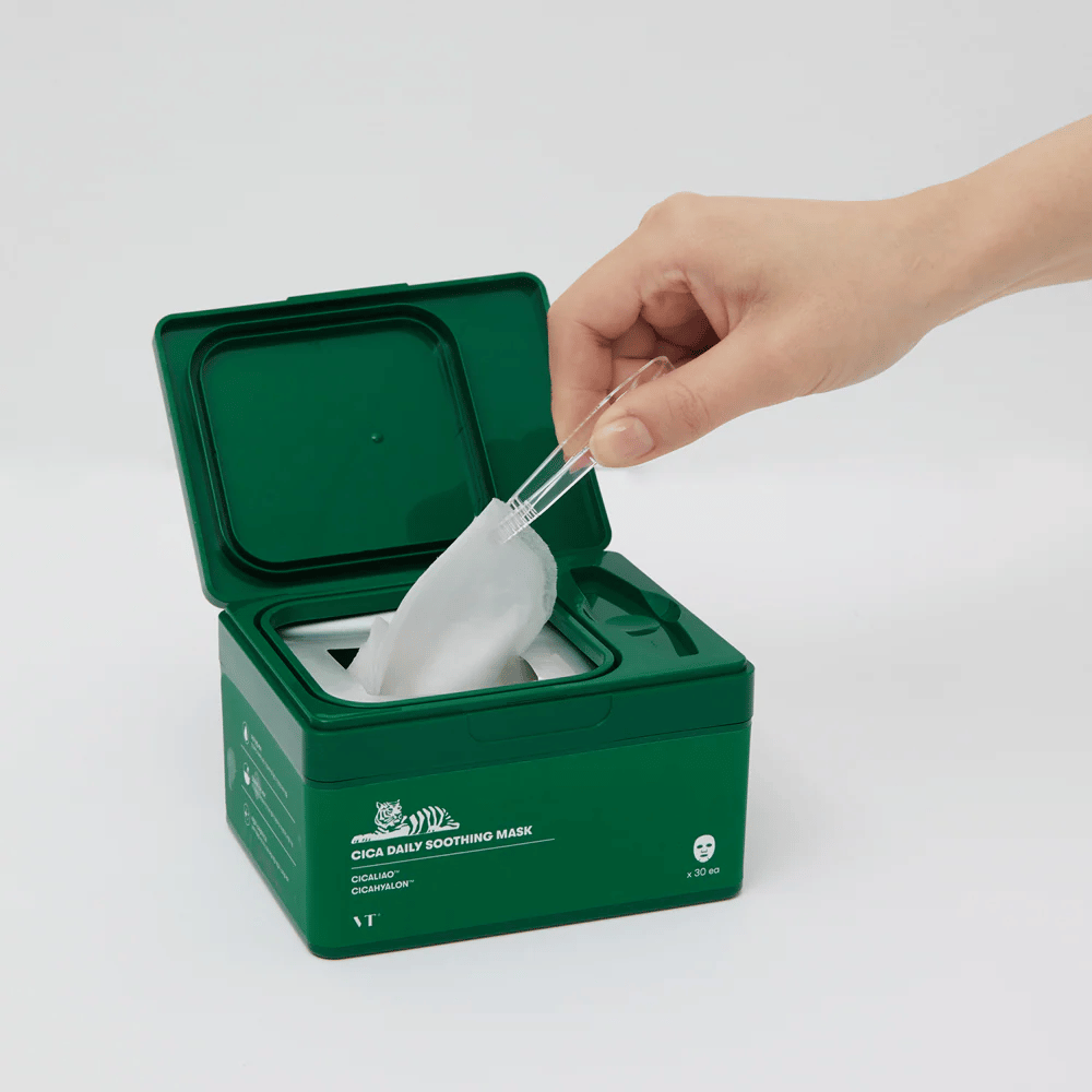 Hand verwendet eine Pinzette, um eine Sheet mask aus einem grünen Behälter zu nehmen, der mit "Cica Daily Soothing Mask" gekennzeichnet ist.