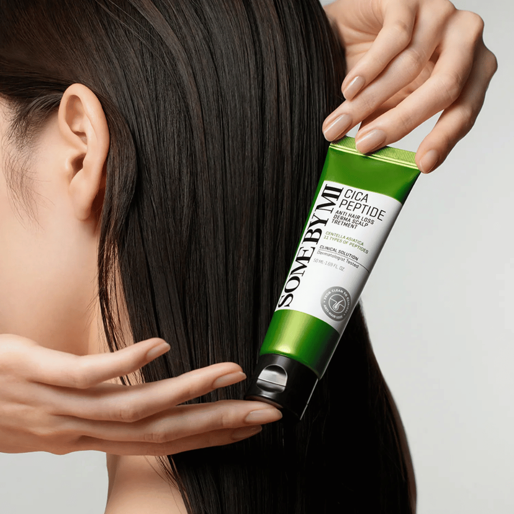 Frau trägt SOME BY MI Cica Peptide Anti Hair Loss Derma Scalp Treatment in langem, dunklem Haar mit einer grünen und weißen Tube auf.