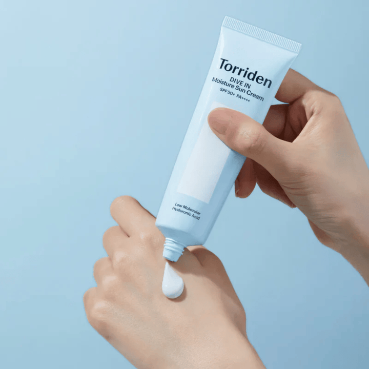 Torriden DIVE-IN Moisture Sun Cream SPF50+ PA++++ wird auf die Hand aufgetragen, um die leichte und cremige Konsistenz der feuchtigkeitsspendenden Sonnencreme zu zeigen.