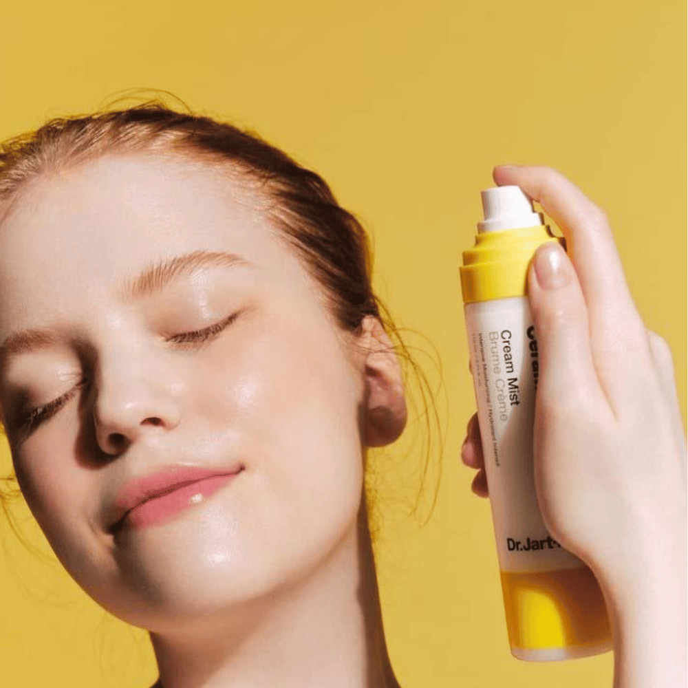 Eine Frau hält eine Flasche Dr. Jart+ Ceramidin Cream Mist 110ml vor ihr Gesicht, was ihre Feuchtigkeits-Boost-Vorteile und vegane Formulierung fördert.