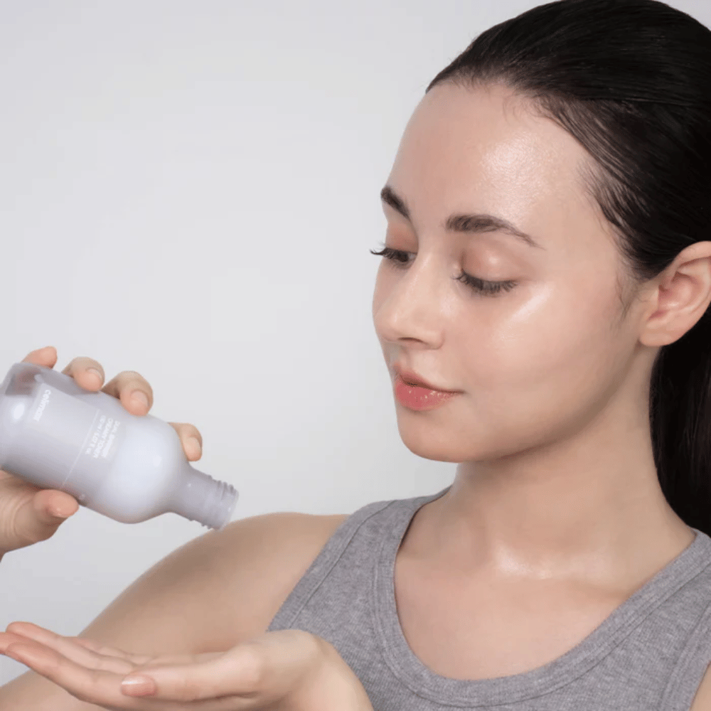Frau mit glänzender, mit Feuchtigkeit versorgter Haut trägt Celimax Dual Barrier Creamy Toner auf, indem sie das Produkt in die Handfläche gießt, bevor sie ihre Hautpflegeroutine beginnt.