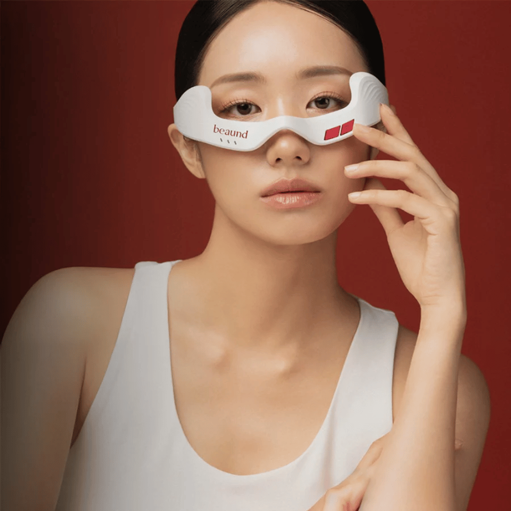 Modellbild, auf dem eine Person Beaund Eye Rejuv verwendet, ein futuristisches LED-Gerät für den Bereich rund um die Augen, vor elegantem rotem Hintergrund.