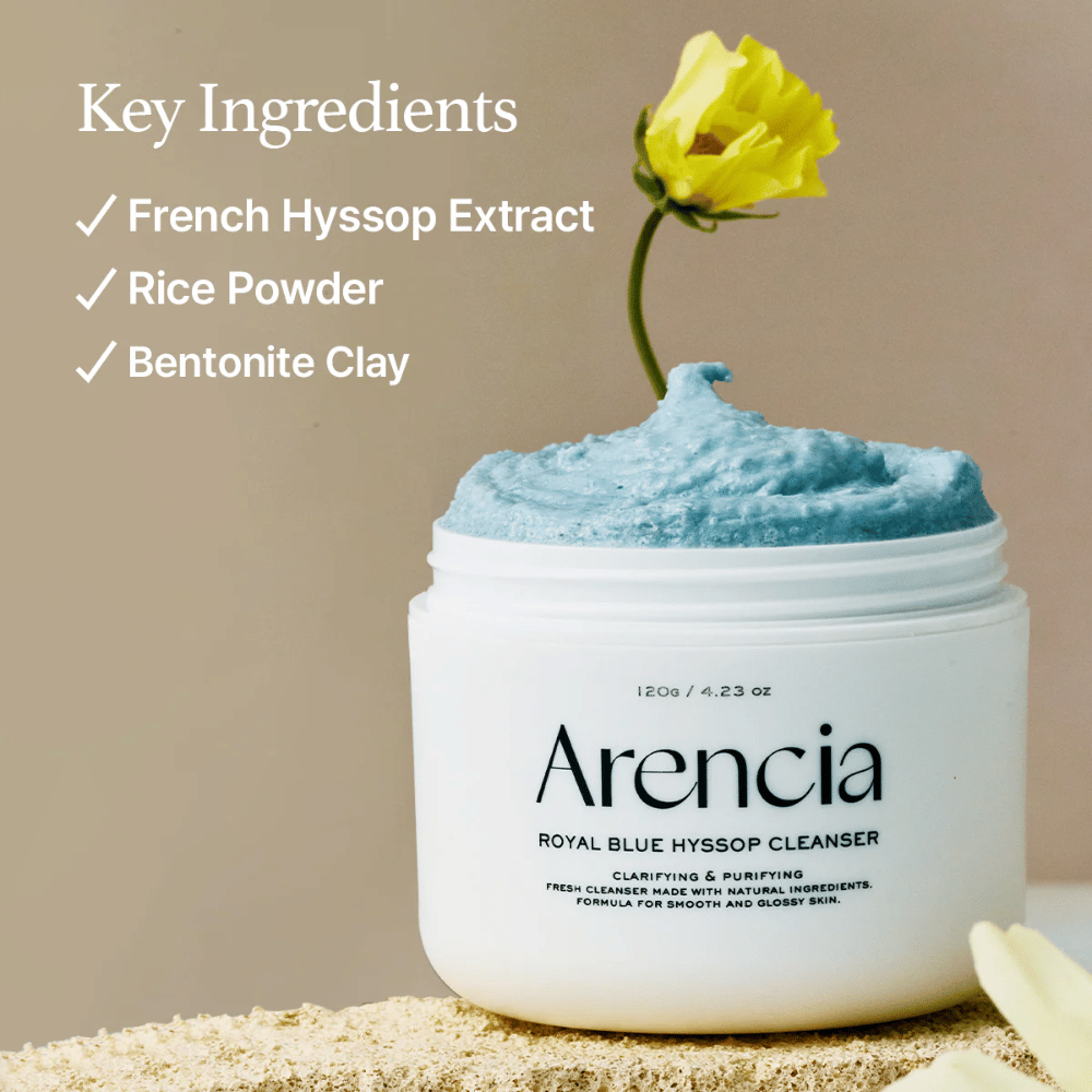 Bild des Glases "Arencia Royal Blue Hyssop Cleanser" gefüllt mit blauer Reinigungspaste. Eine gelbe Blume ragt aus der Paste heraus. Der Text im Bild hebt drei Schlüsselzutaten hervor: Französischer Ysop-Extrakt, Reispulver und Bentonit-Ton.