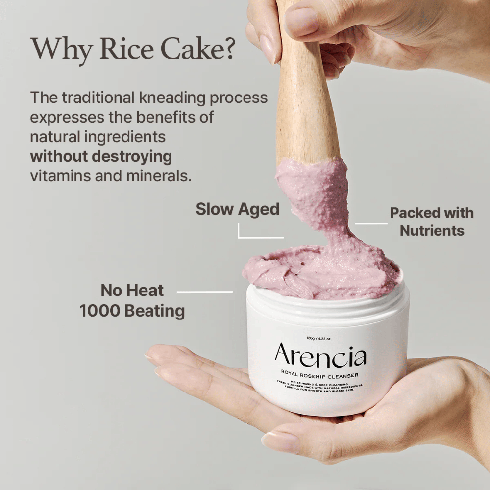 Eine Hand hält ein geöffnetes Gefäß von Arencia Royal Rosehip Cleanser, mit einer rosa, mochi-ähnlichen Reinigungsformel, die mit einem Holzspatel gehoben wird – zeigt die Textur des Produkts und die traditionelle Herstellungsmethode.