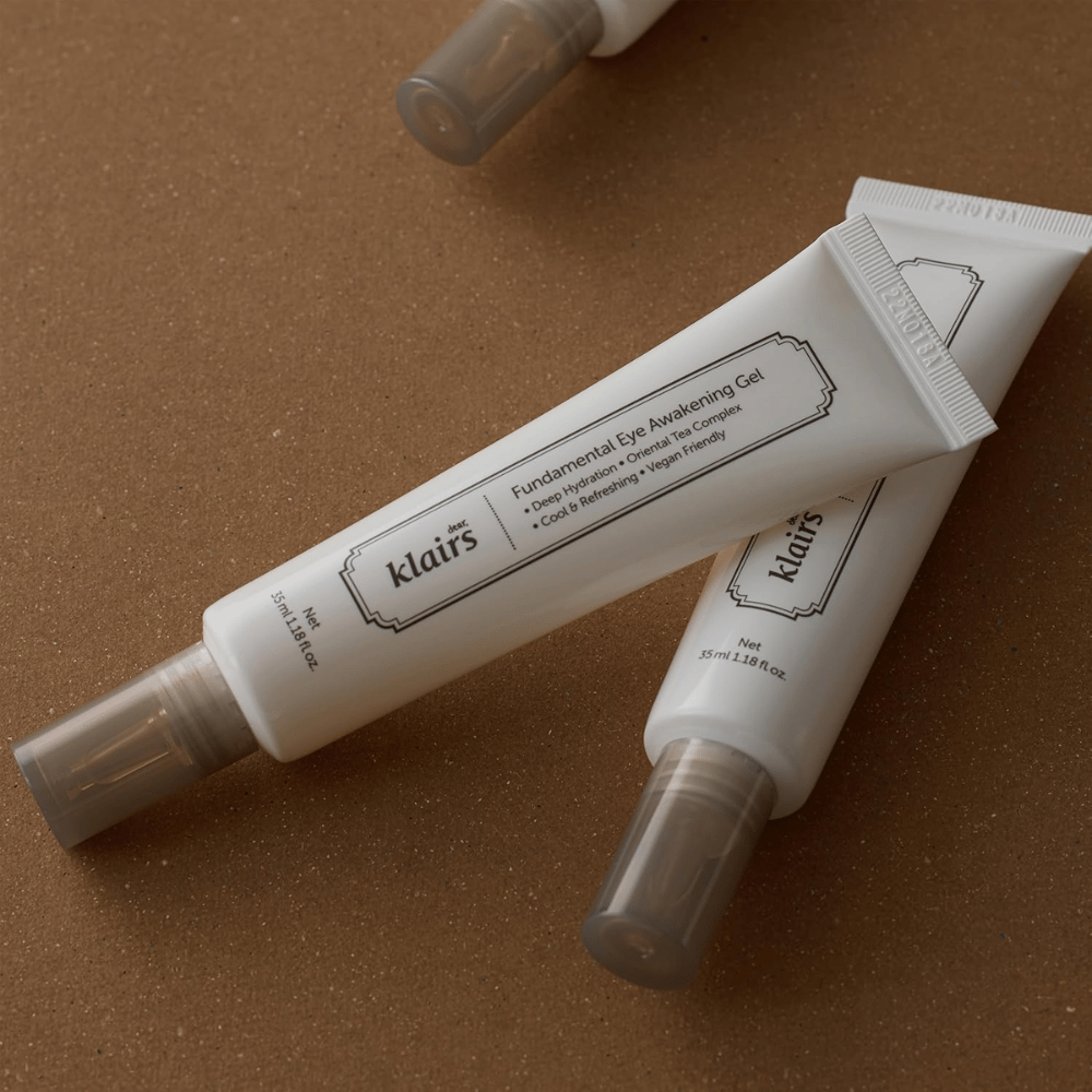 Lifestyle-Bild mit zwei Tuben von Klairs Fundamental Eye Awakening Gel, platziert vor einem warmen braunen Hintergrund. Die Komposition hebt das elegante Design und das Premium-Gefühl des Produkts hervor, während der Fokus auf Augenpflege und Feuchtigkeit liegt.