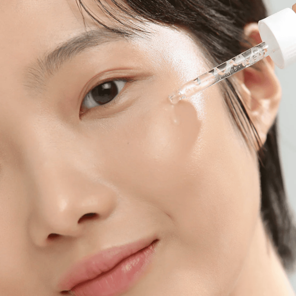 Nahaufnahme einer Frau, die Serum mit einer Pipette auf die Wange aufträgt – Hautpflege, die Glow und Feuchtigkeit spendet.