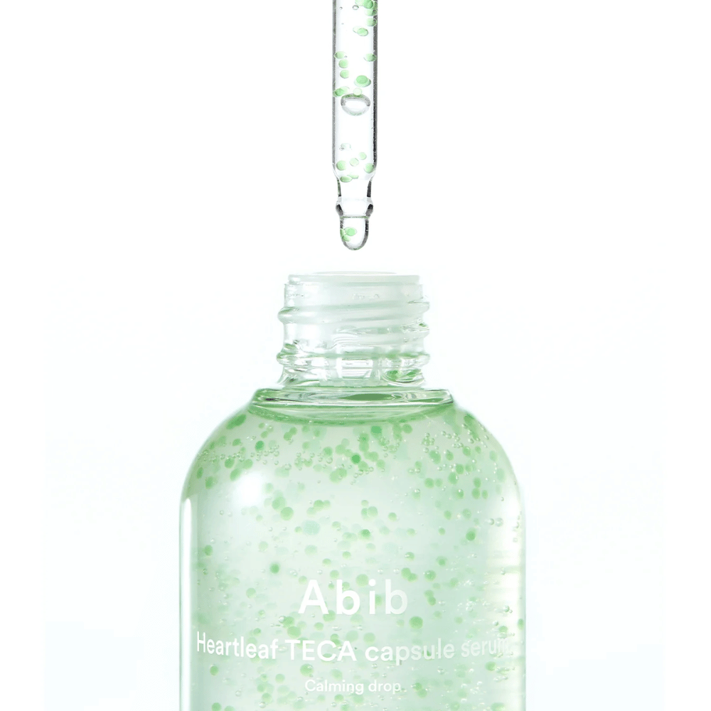 Minimalistische Nahaufnahme einer Serumflasche und Pipette, bei der die transparente Formel mit grünen Kapseln vor hellem Hintergrund im Fokus steht.
