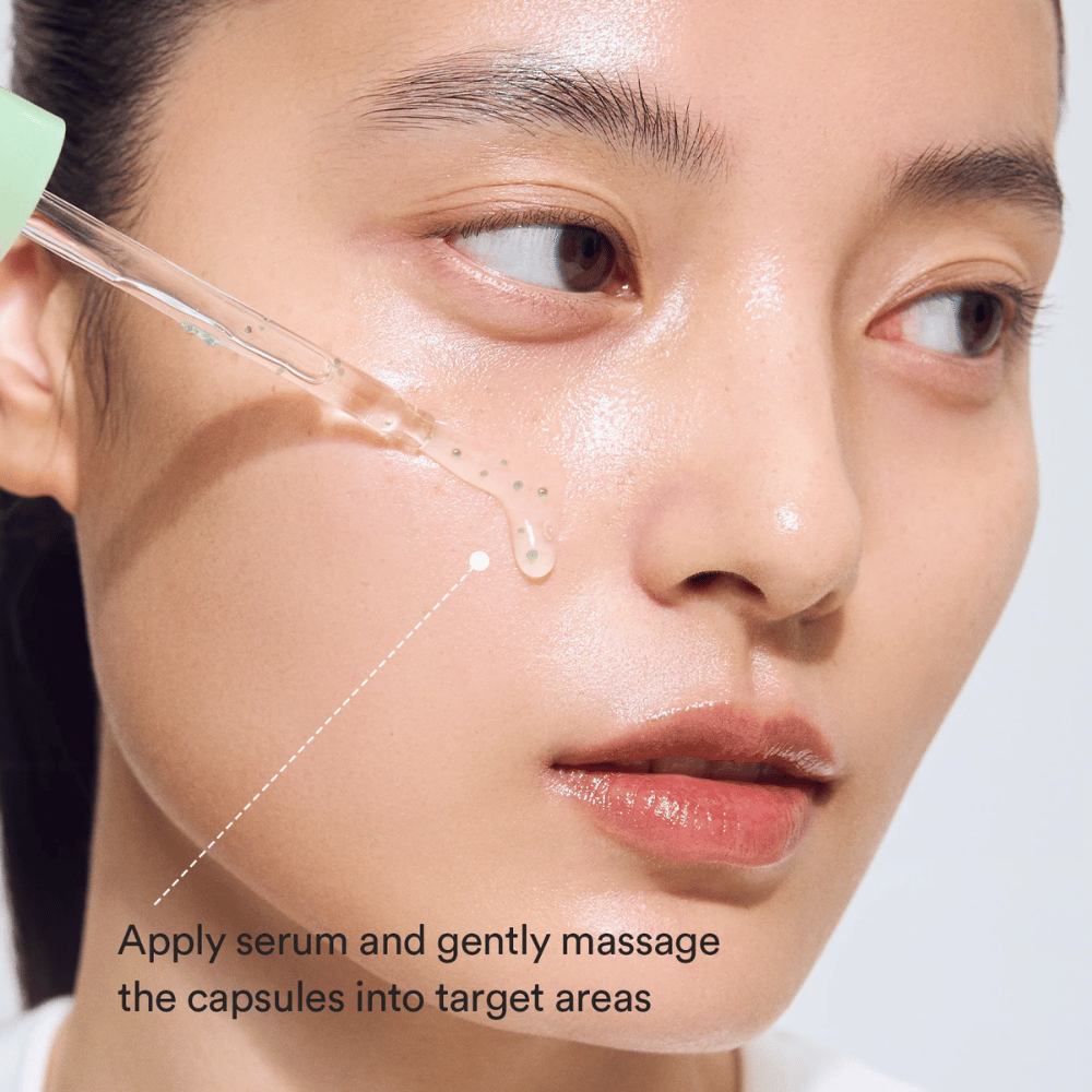 Nahaufnahme eines Models, das das Serum mit einer Pipette aufträgt, während die grünen Kapseln für eine beruhigende und feuchtigkeitsspendende Wirkung in die Haut einmassiert werden.