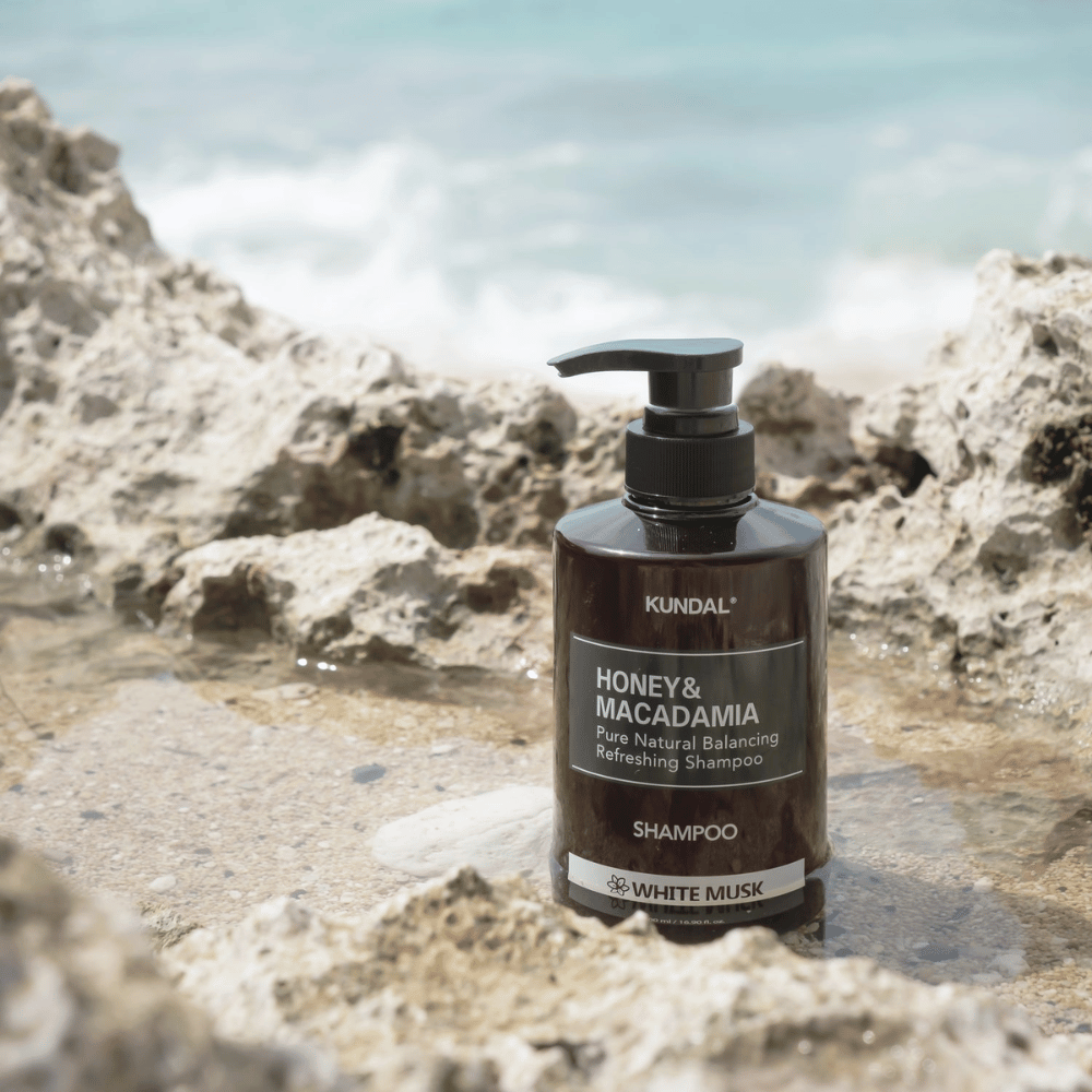 KUNDAL Honey & Macadamia Nature Shampoo White Musk auf Felsen am Meer platziert, ein natürliches Haarpflegeprodukt mit frischem Duft.