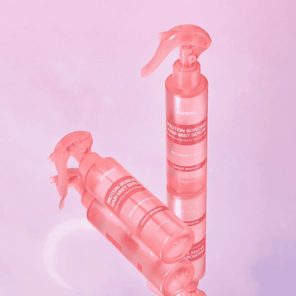 KUNDAL Protein Bonding Hair Mist Serum Violet Muguet in rosa Sprühflaschen, stehend und liegend vor einem hellrosa Hintergrund mit Reflexion.