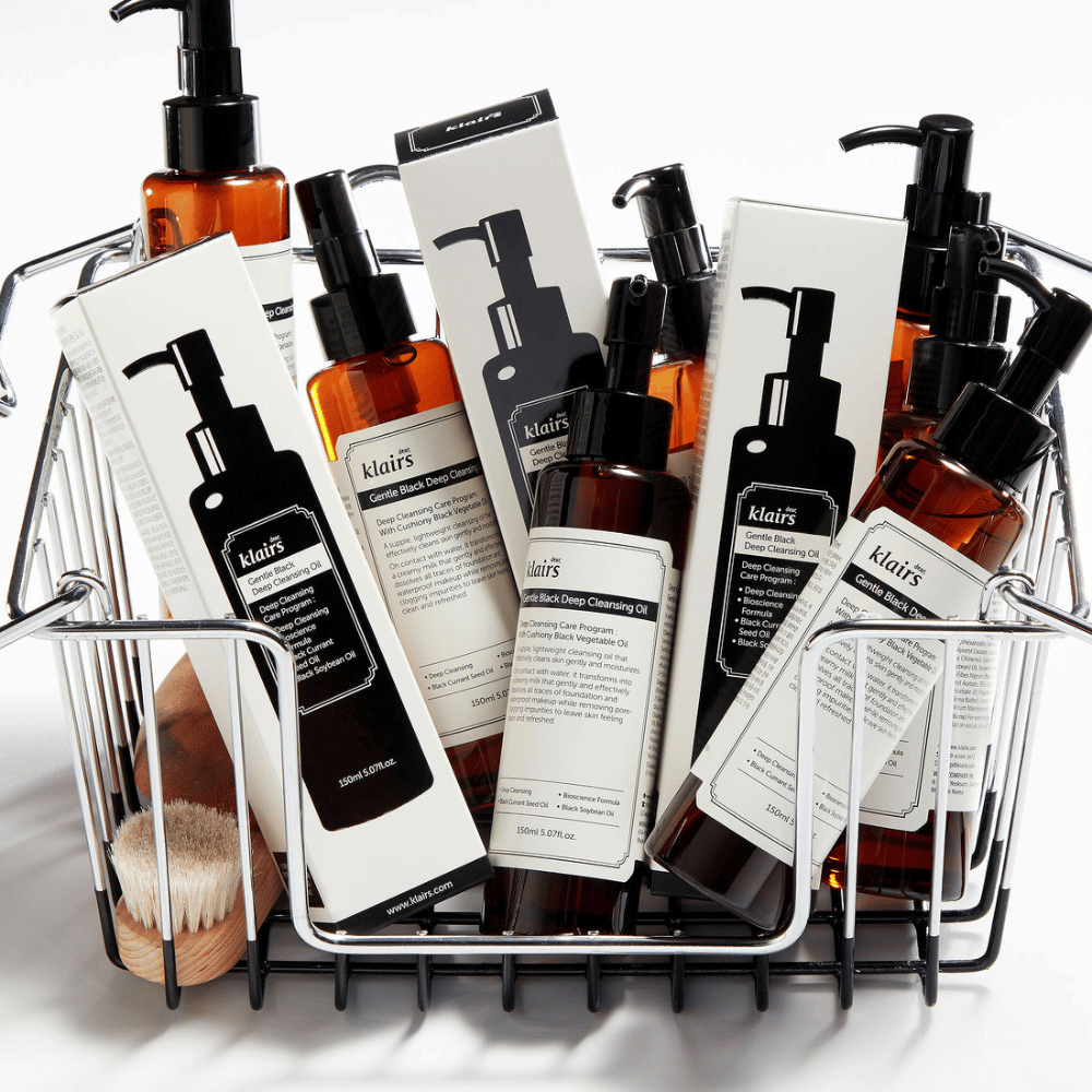 Ein Mini-Einkaufswagen gefüllt mit Hautpflegeprodukten von Klairs, einschließlich Gentle Black Deep Cleansing Oil in durchsichtigen Flaschen mit schwarzen Pumpen und passenden Verpackungen.