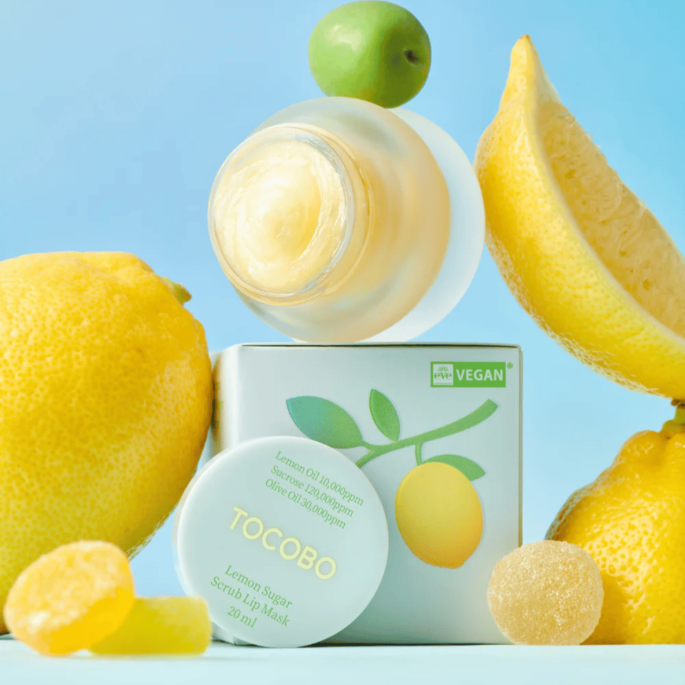 Dose mit Tocobo Lemon Sugar Scrub Lip Mask zwischen Zitronen und Verpackung platziert, als veganfreundlich markiert.