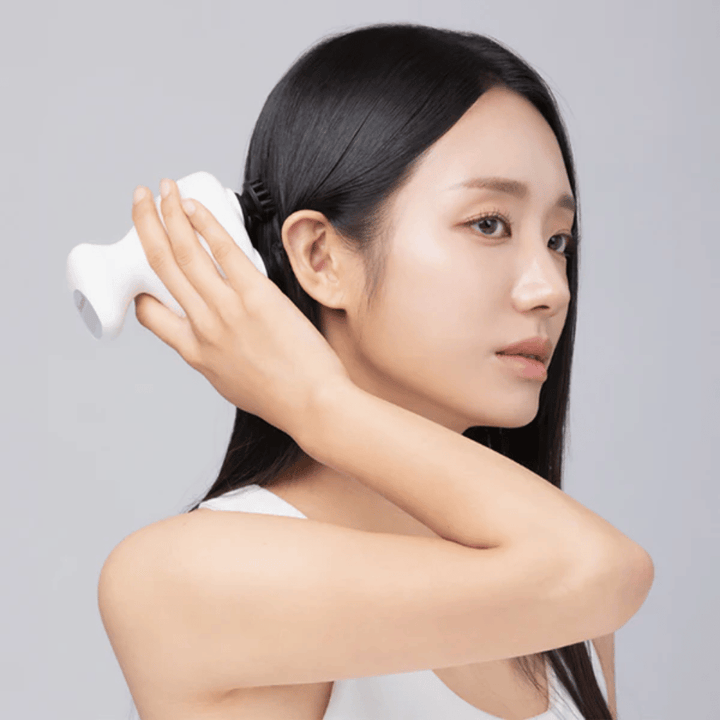 Ein Modell verwendet Beaund Lift Head Spa direkt auf der Kopfhaut hinter dem Ohr. Das Bild demonstriert, wie das Gerät zur Massage der Kopfhaut verwendet wird und eine angenehme Stimulation bietet.