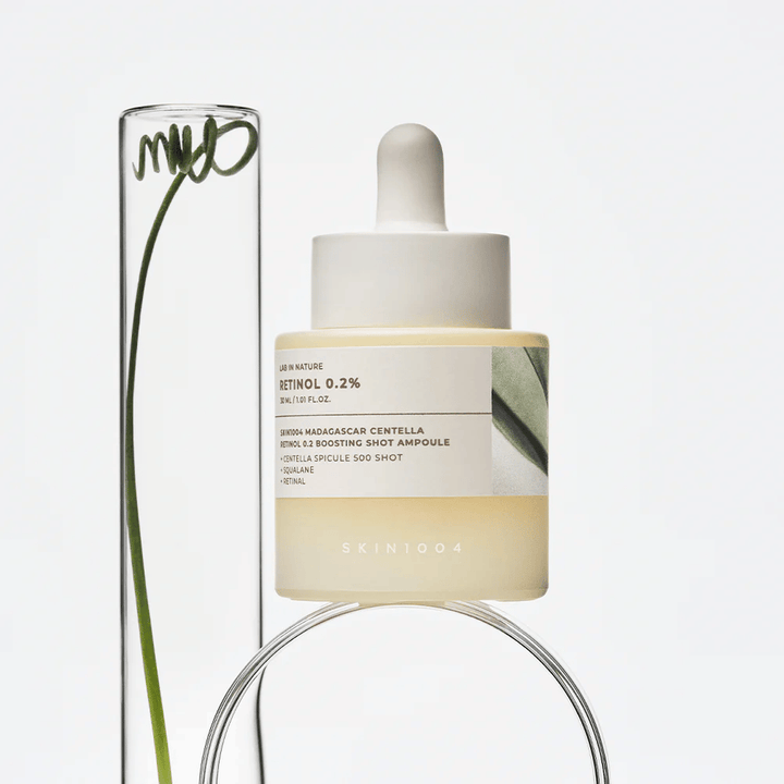 SKIN1004 Madagascar Centella Retinol 0.2 Boosting Shot Ampoule in einem Lifestyle-Bild mit botanischen Elementen – ein Gesichtsserum, das die Hauterneuerung unterstützt und die Hautbarriere stärkt.