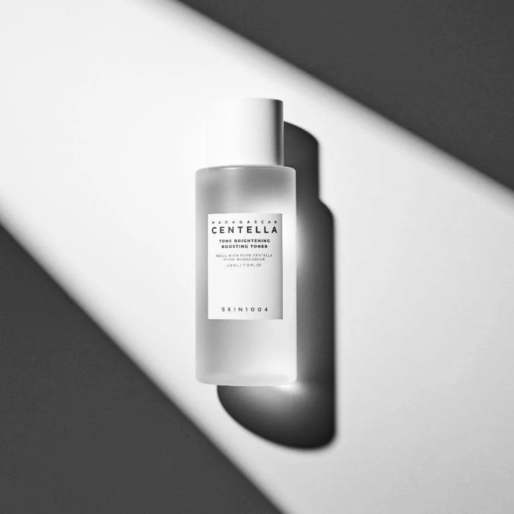 Flasche von SKIN1004 Madagascar Centella Tone Brightening Boosting Toner  liegend auf weißer Oberfläche mit dramatischem Schatten im Schwarz-Weiß-Lichtspiel.