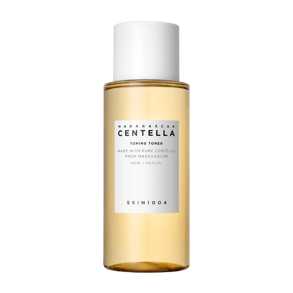 Das Bild zeigt eine Flasche mit Hautpflegetoner, gekennzeichnet mit "Madagascar Centella Toning Toner" von SKIN1004. Das Produkt soll 210 ml oder 7,10 fl.oz enthalten und wird mit reiner Centella aus Madagaskar hergestellt. Die Verpackung ist einfach und elegant mit einer transparenten Flasche und goldfarbener Tonerflüssigkeit im Inneren, was ein Gefühl von Luxus und Reinheit vermittelt. Das Markenlogo SKIN1004 ist deutlich sichtbar im unteren Teil des Etiketts.