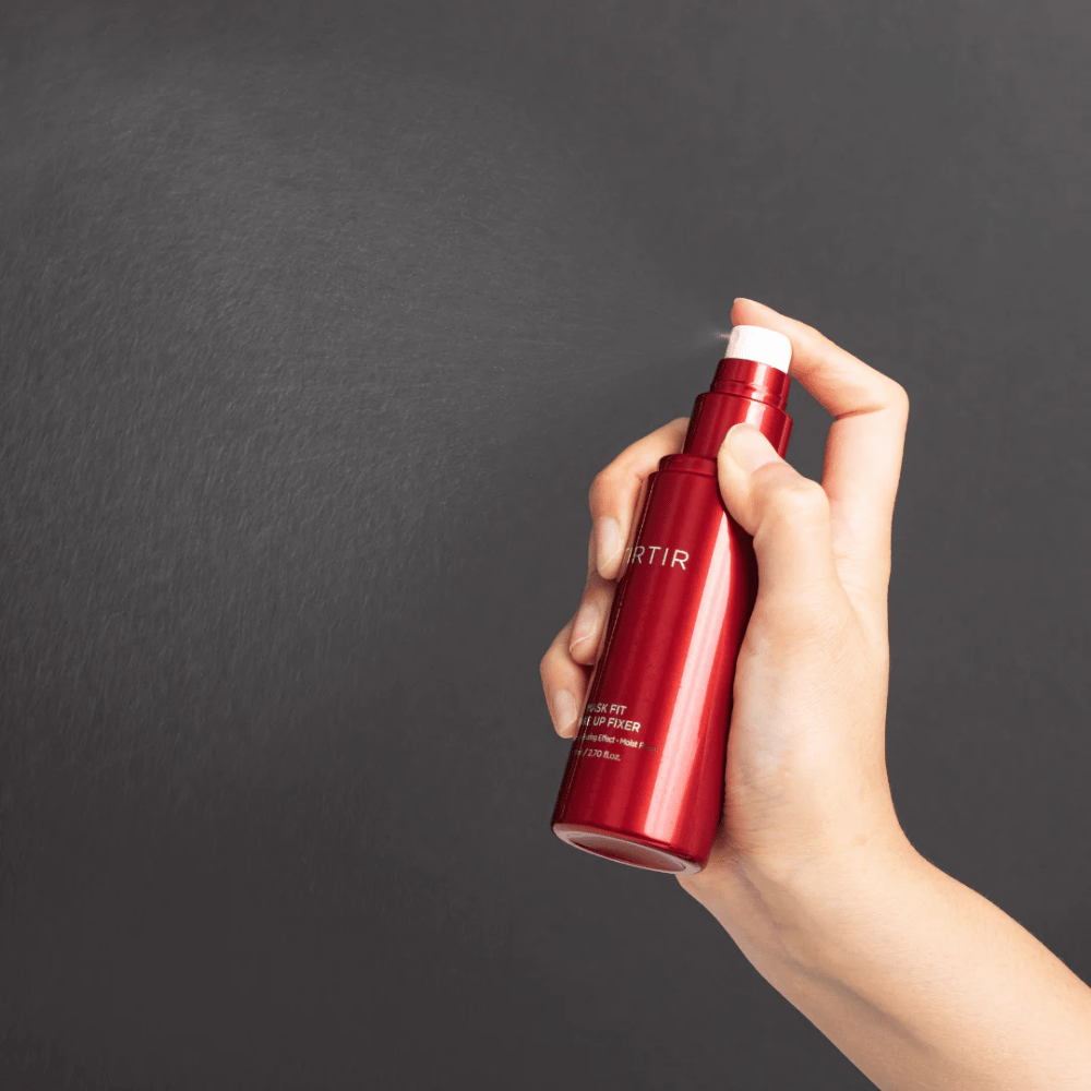Eine Hand hält eine rote Flasche der Marke tirtir Mask Fit Make Up Fixer und sprüht einen feinen Nebel, ideal zur Fixierung von Make-up.