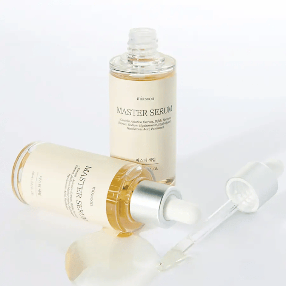 Zwei Flaschen Mixsoon Master Serum, eine stehend und eine liegend mit offener Pipette, wobei das Serum auf eine weiße Oberfläche verschüttet wurde.