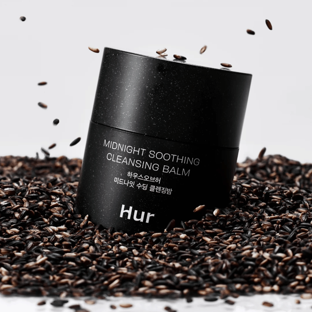 Wie Midnight Soothing Cleansing Balm in schwarzer Dose auf schwarzen Samen platziert. Beruhigender Reinigungsbalsam, der Make-up und Unreinheiten löst und gleichzeitig die Haut pflegt.