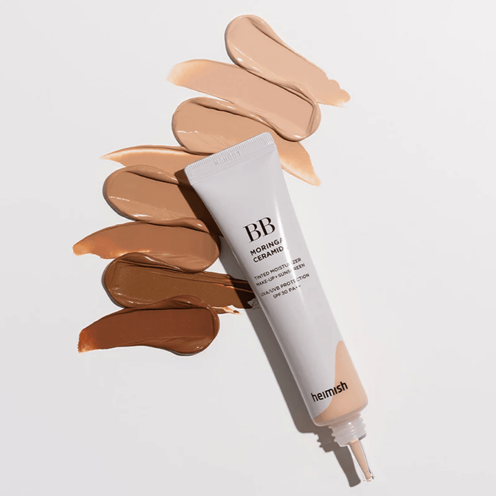 Heimish Moringa Ceramide BB Cream, umgeben von mehreren Farbmuster in verschiedenen Hauttönen. Das Bild zeigt die breite Farbpalette des Produkts und die cremige Konsistenz, die eine natürliche Deckkraft und einen ebenmäßigen Hautton verleiht.