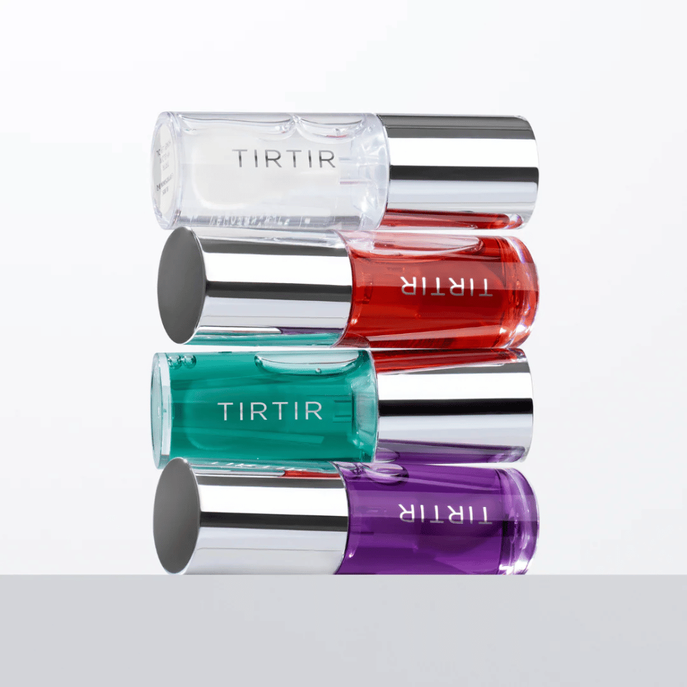 Vier TIRTIR My Glow Lip Oil in verschiedenen Farben – transparent, rot, grün und lila – übereinander gestapelt mit silberfarbenen Deckeln gegen weißen Hintergrund.