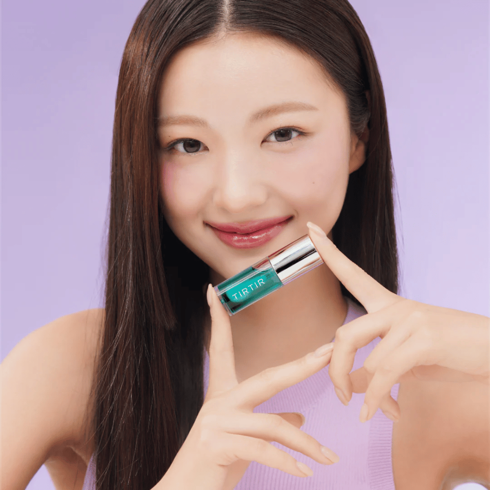 Frau mit langem, glattem Haar hält TIRTIR My Glow Lip Oil und zeigt ihre glänzenden, rosa Lippen vor einem lila Hintergrund.