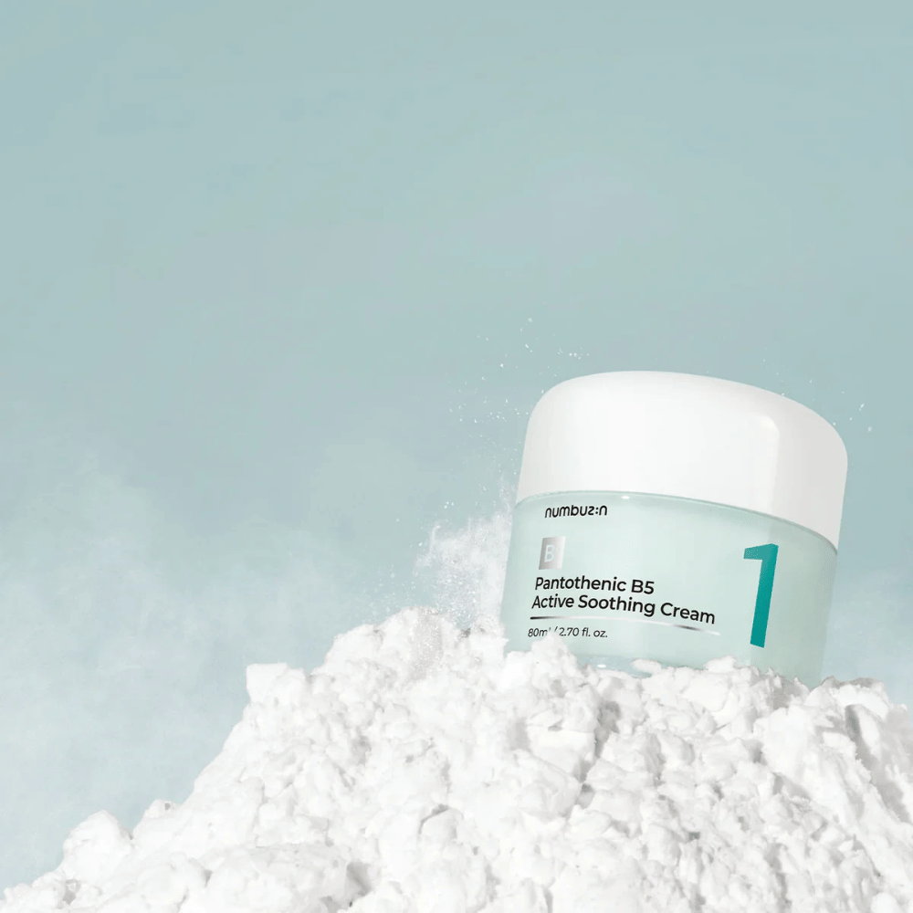 Numbuzin No.1 Pantothenic B5 Active Soothing Cream 80 ml in hellgrünem Behälter mit weißem Deckel, platziert auf einem Haufen weißen Pulvers vor einem hellen Hintergrund.