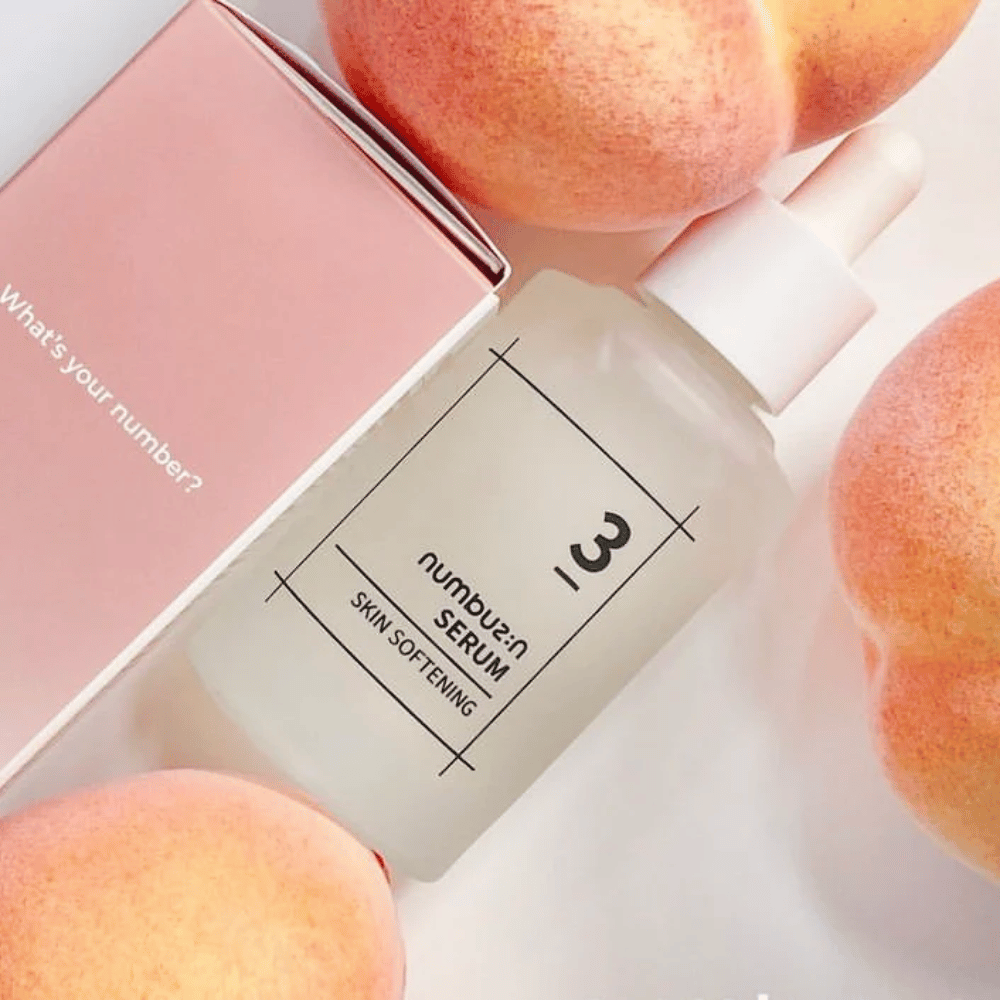 Flasche mit numbus:in No.3 Skin Softening Serum umgeben von Pfirsichen und einer rosa Schachtel mit dem Text "What's your number?".