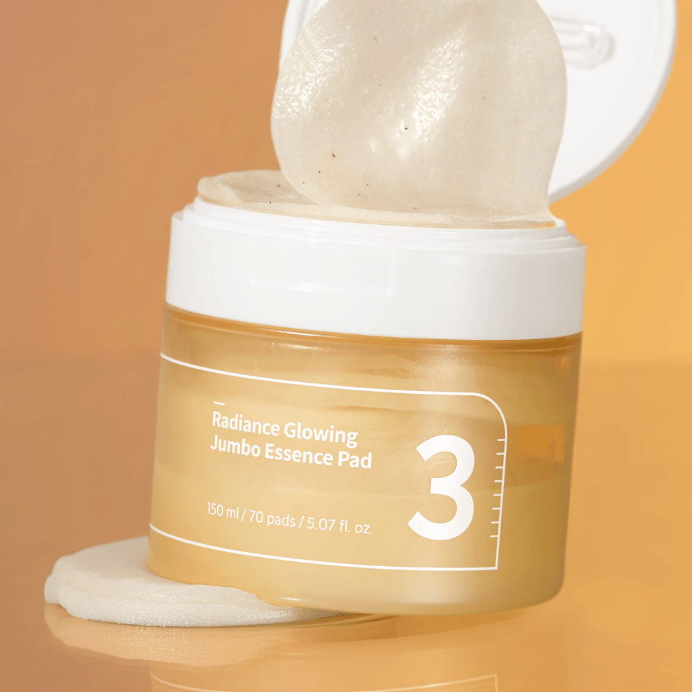 Offene Dose mit numbuzin No. 3 Radiance Glowing Jumbo Essence Pad, ein Pad lehnt an der Kante, Hintergrund in Orangetönen.