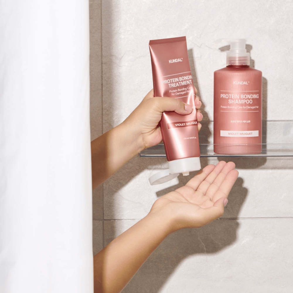 KUNDAL Protein Bonding Treatment Violet Muguet wird in der Dusche verwendet, mit Protein Bonding Shampoo auf dem Regal daneben platziert.