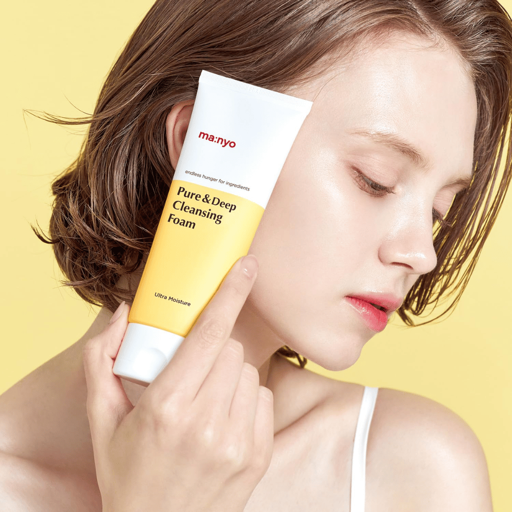 Frau mit gesunder, mit Feuchtigkeit versorgter Haut hält Ma:nyo Pure & Deep Cleansing Foam – milde Gesichtsreinigung, die mit natürlichen Inhaltsstoffen Glanz und Balance verleiht.