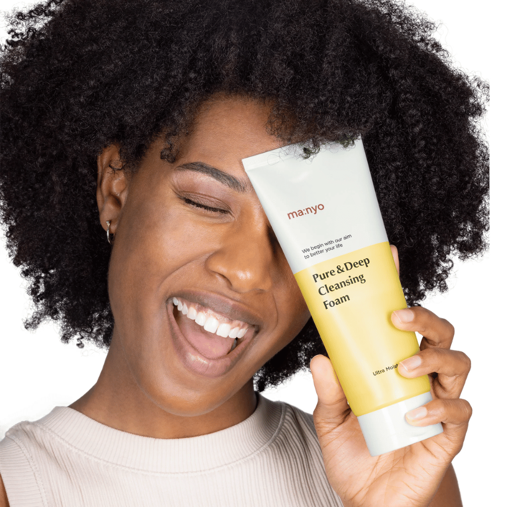 Frau mit lockigem Haar hält Ma:nyo Pure & Deep Cleansing Foam – eine sanfte koreanische Reinigung, die effektiv Schmutz und Make-up entfernt, ohne die Haut auszutrocknen.