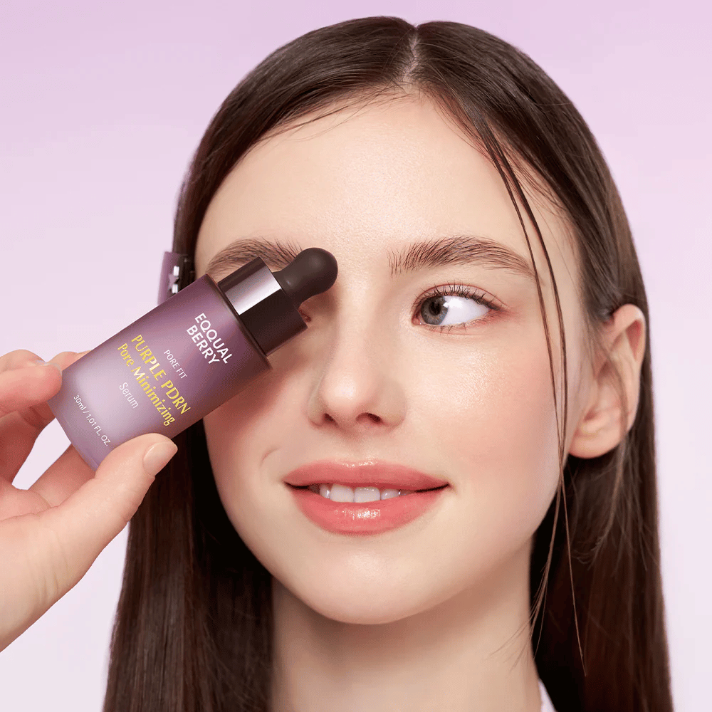 Junge Frau mit glatter Haut hält eine Flasche Equal Berry Purple PDRN Pore Minimizing Serum an ihre Stirn, vor einem helllila Hintergrund.